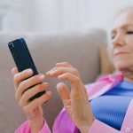 Older woman lying on couch with smartphone in her hand