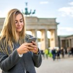 Blonde young girl using phone in front of Brandenburger Tor