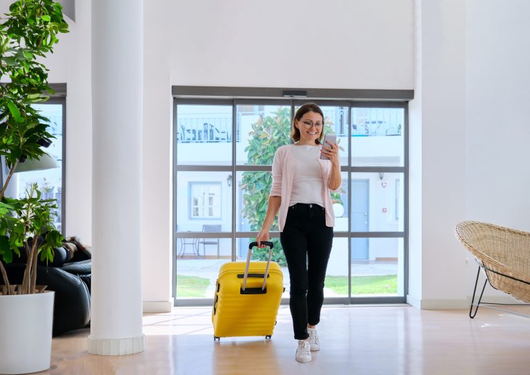 Woman with smartphone walking into hotel lobby smiiling